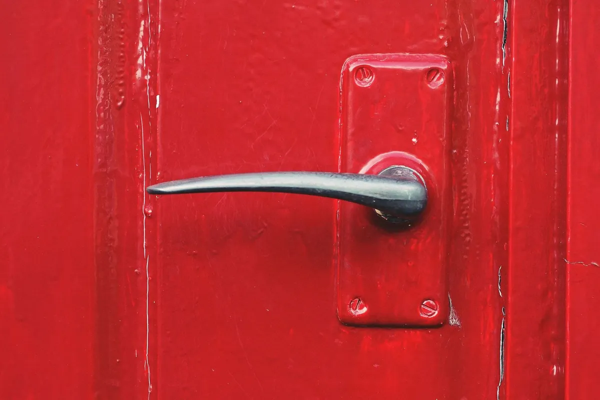 A close-up of a bright red door with a metallic handle, symbolizing an inviting entrance for a quick home sale.